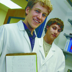 Two wearing white lab coats, one holding a clipboard