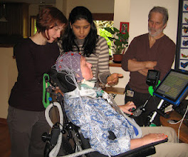 two women and a man standing around a person in a wheelchair with an electrode cap on