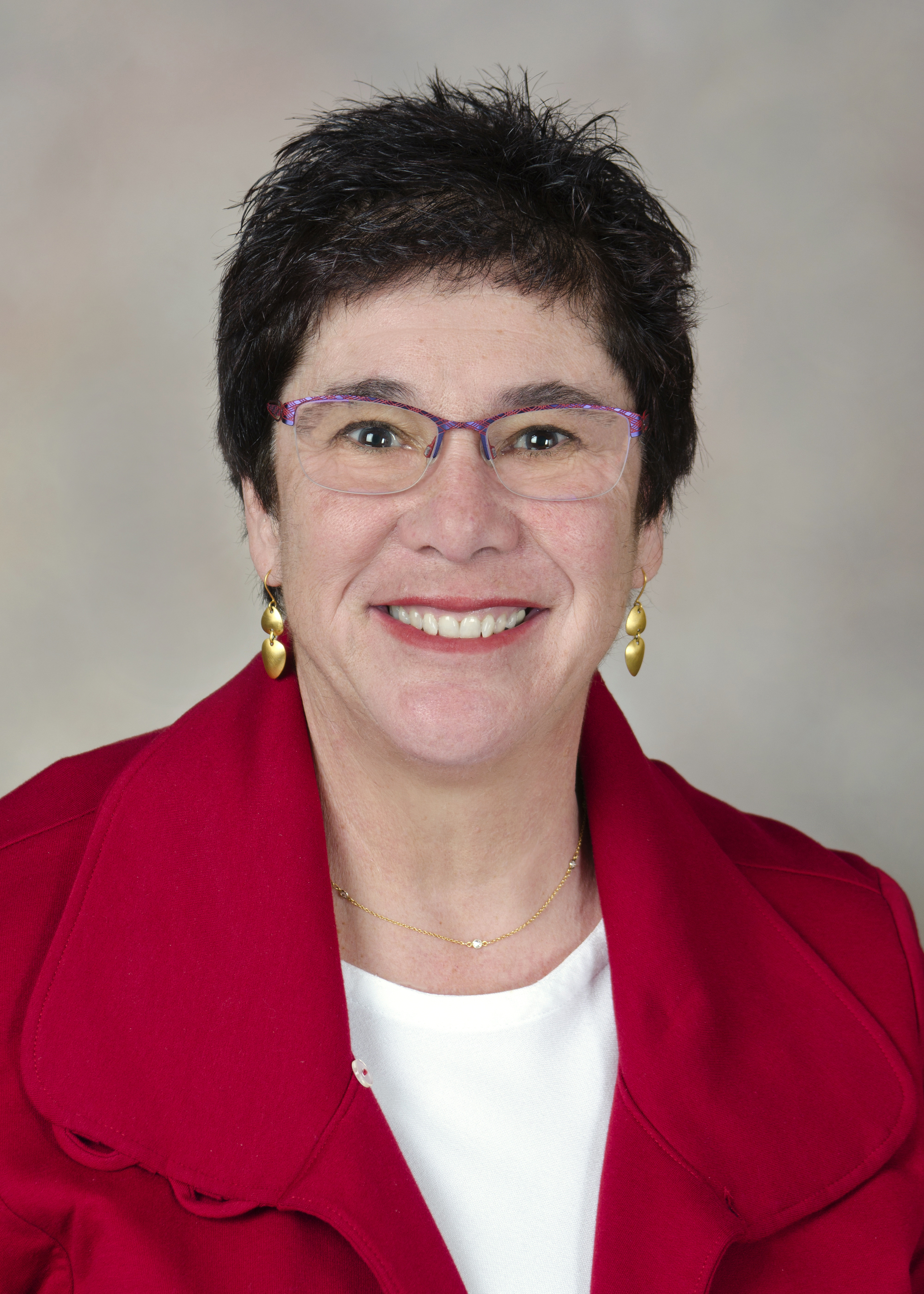 This is an image of Dr. Melanie Fried-Oken, a smiling woman in her 60's with short dark hair and a red jacket.