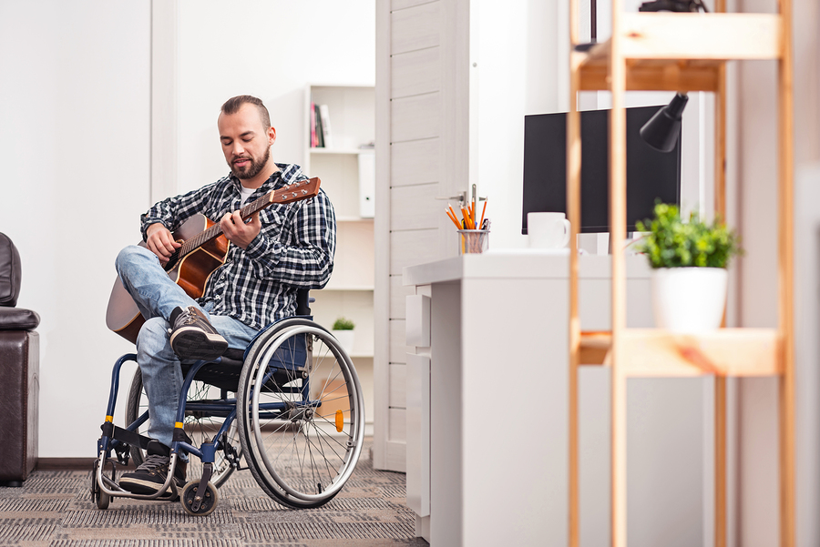 Man in a wheelchair playing guitar in a small apartment