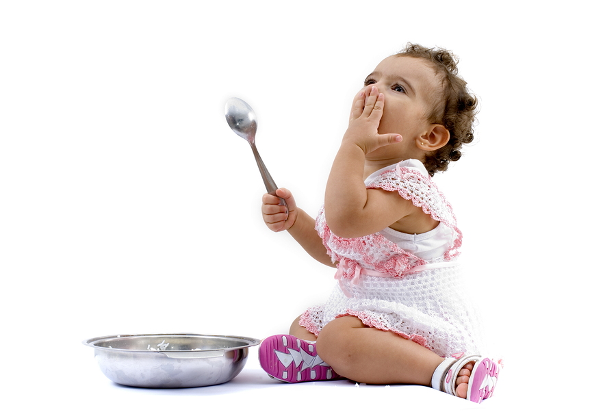 Toddler girl sitting on the floor eating from a bowl