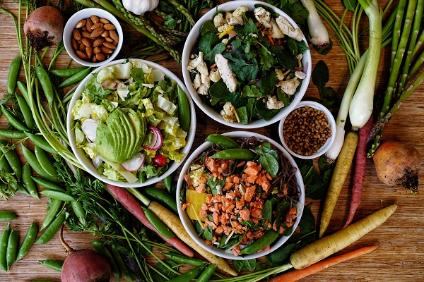 Fresh Salads with nuts and seeds in bowls surrounded by veggies laying on a table