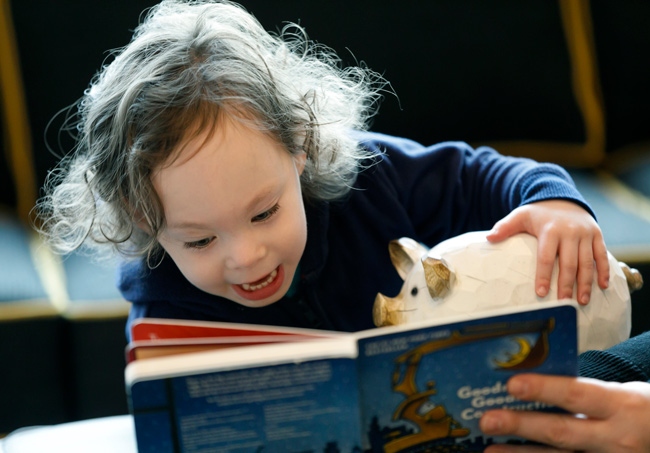 A child at play, looking at a book and holding a toy pig