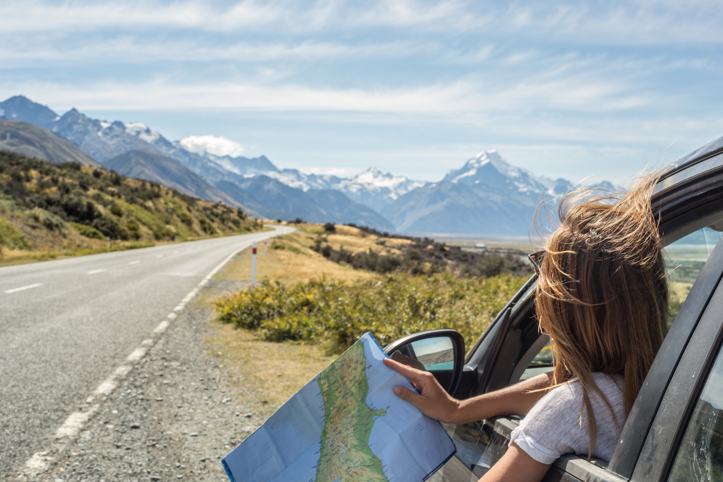 Woman in car looking at a map with mountains in the distance.