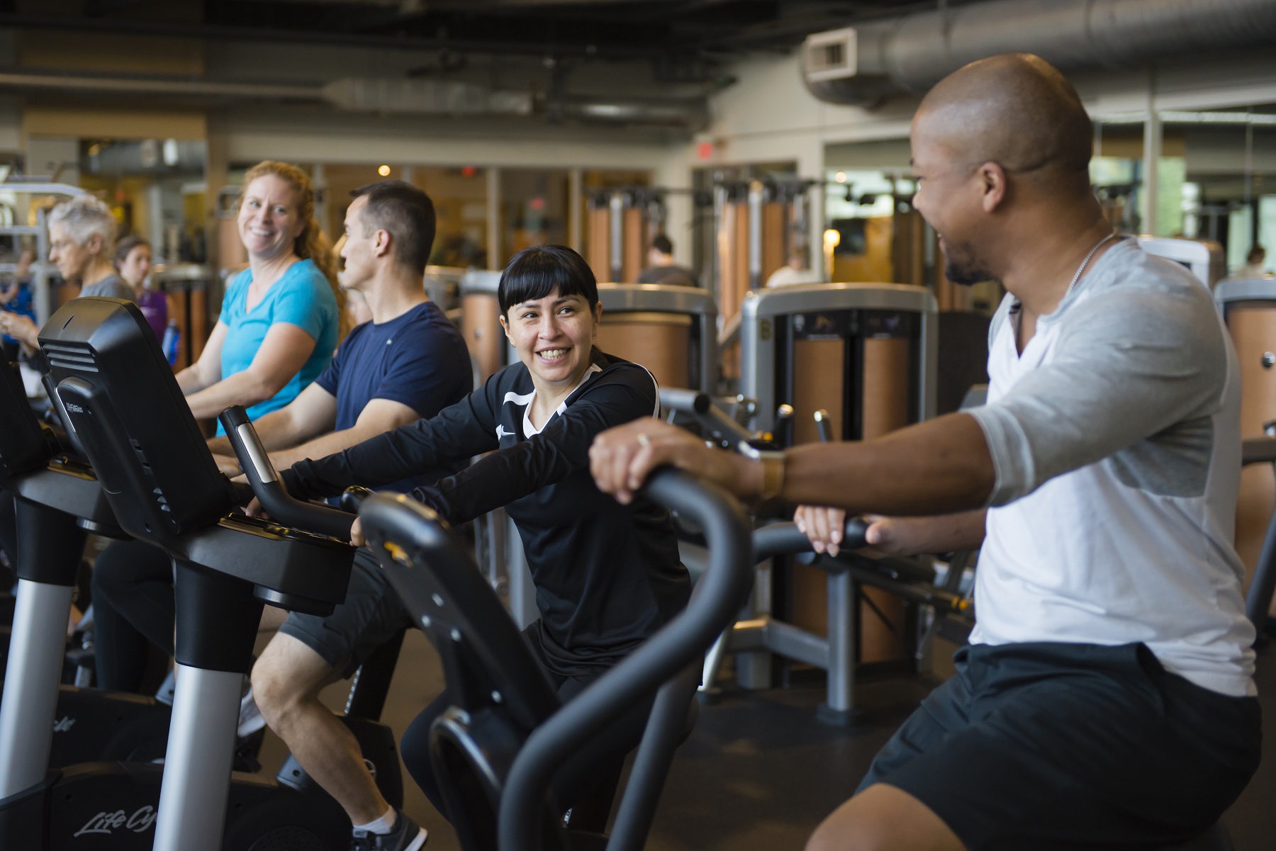 Row of 4 members on stationary bikes on march wellness & fitness center's fitness floor.