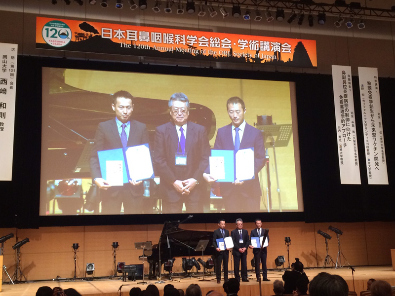 Photo of Takahiro Tsujikawa, M.D., Ph.D., being awarded along with another recipient as best young physician scientist in Japan, by the Otorhinolaryngological Society of Japan.