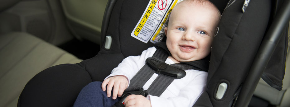 Photo of a baby smiling while fastened into a car seat designed for babies, well-padded with straps.