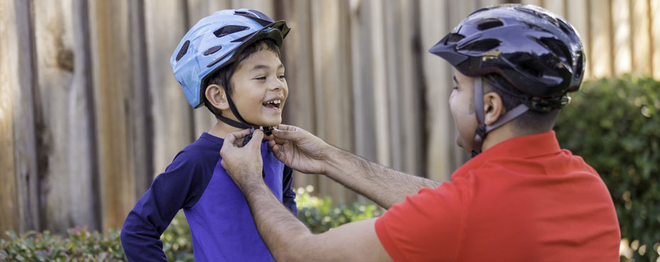 A father helps buckle the bike helmet for his son who is smiling