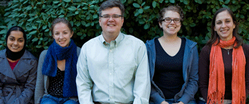 A photo of Anthony Paul Barnes and the four members of his research lab standing outside in front of hedges.