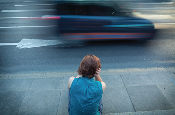 woman sits on sidewalk as traffic rushes by