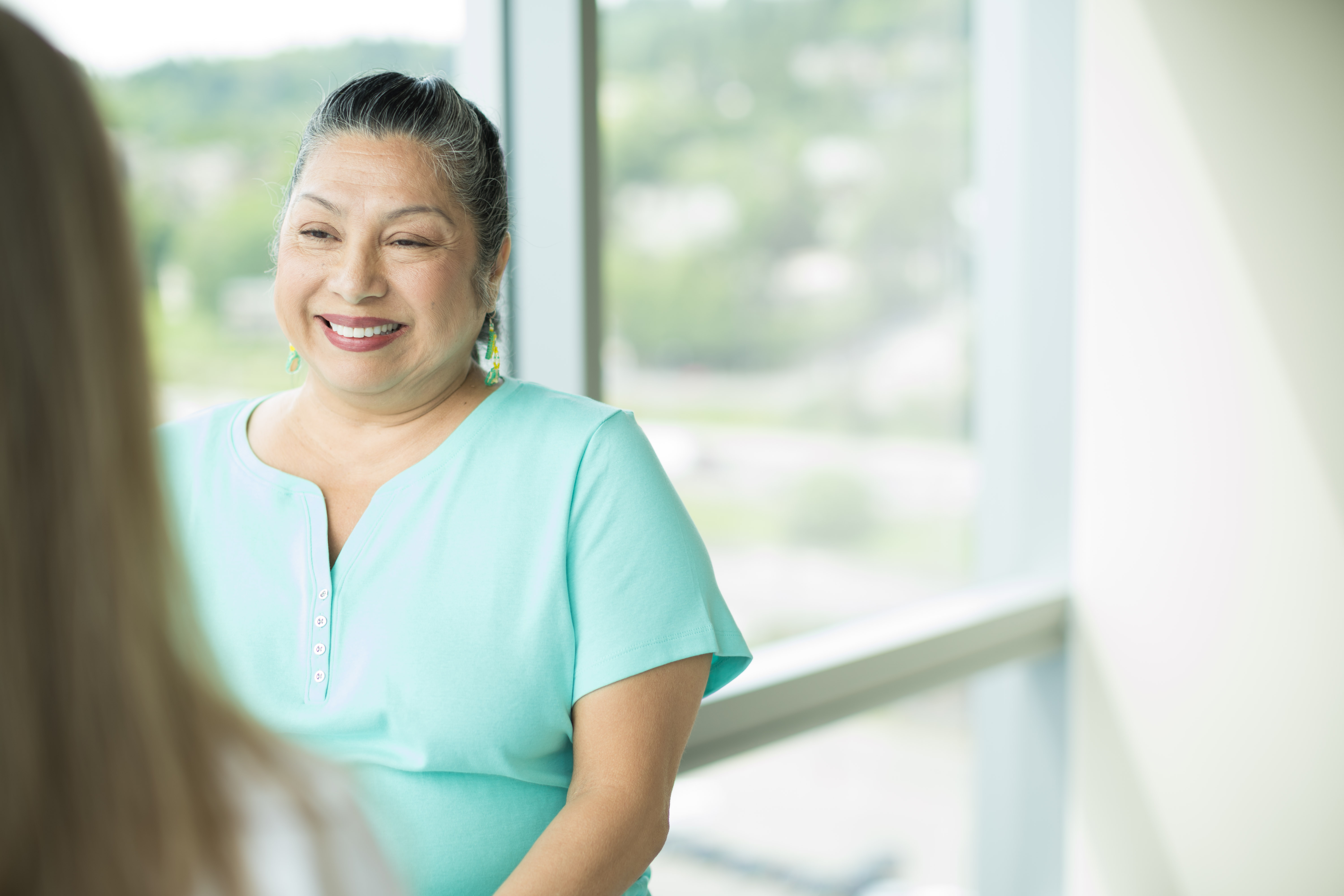 Photograph of a smiling woman in a clinic room with a window. At the OHSU Parkinson Center, patients receive care from a team of experts.