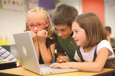 3 Children Looking at a laptop in a classroom