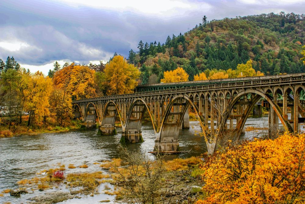 Arch bridge across a river in Oregon in the fall.  Foliage on surrounding trees is yellow and orange.