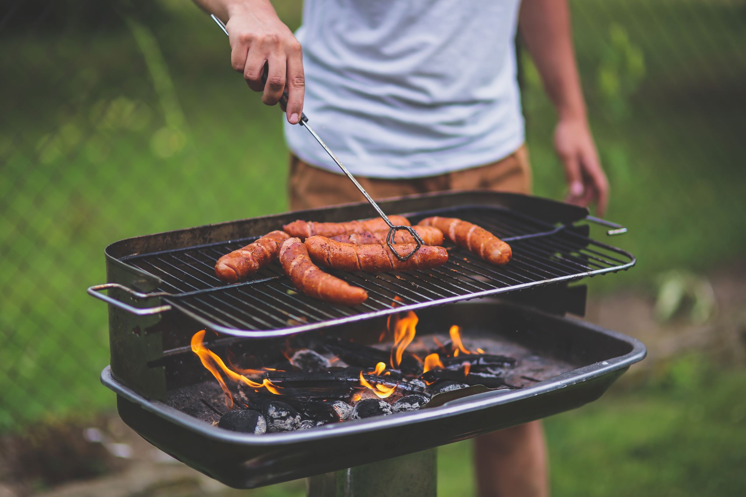 man grilling hot dogs over charcoal grill