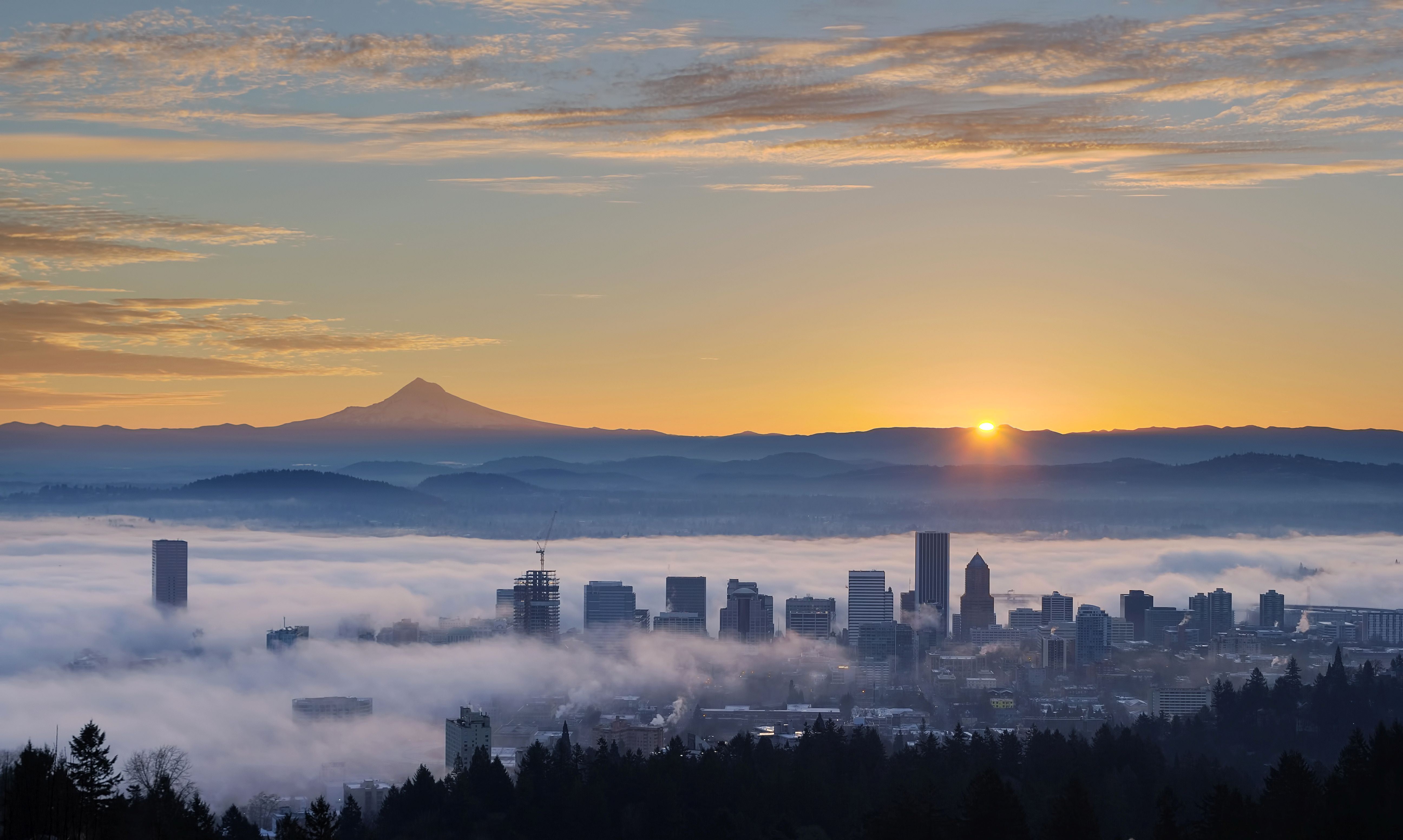 Sunrise view of downtown Portland, OR covered in fog with Mt. Hood in the background.