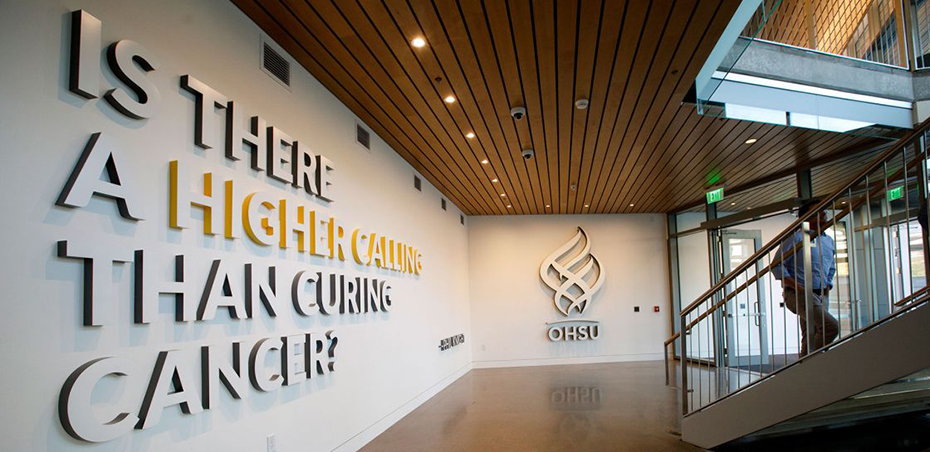 An interior shot of inside the OHSU Knight Cancer Research Building, showing a wall that has the OHSU logo on it, with the words "Is there a higher calling than curing cancer?" next to it.