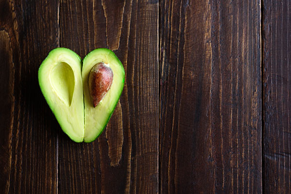 Avocado cut open and arranged in heart shape on wooden surface