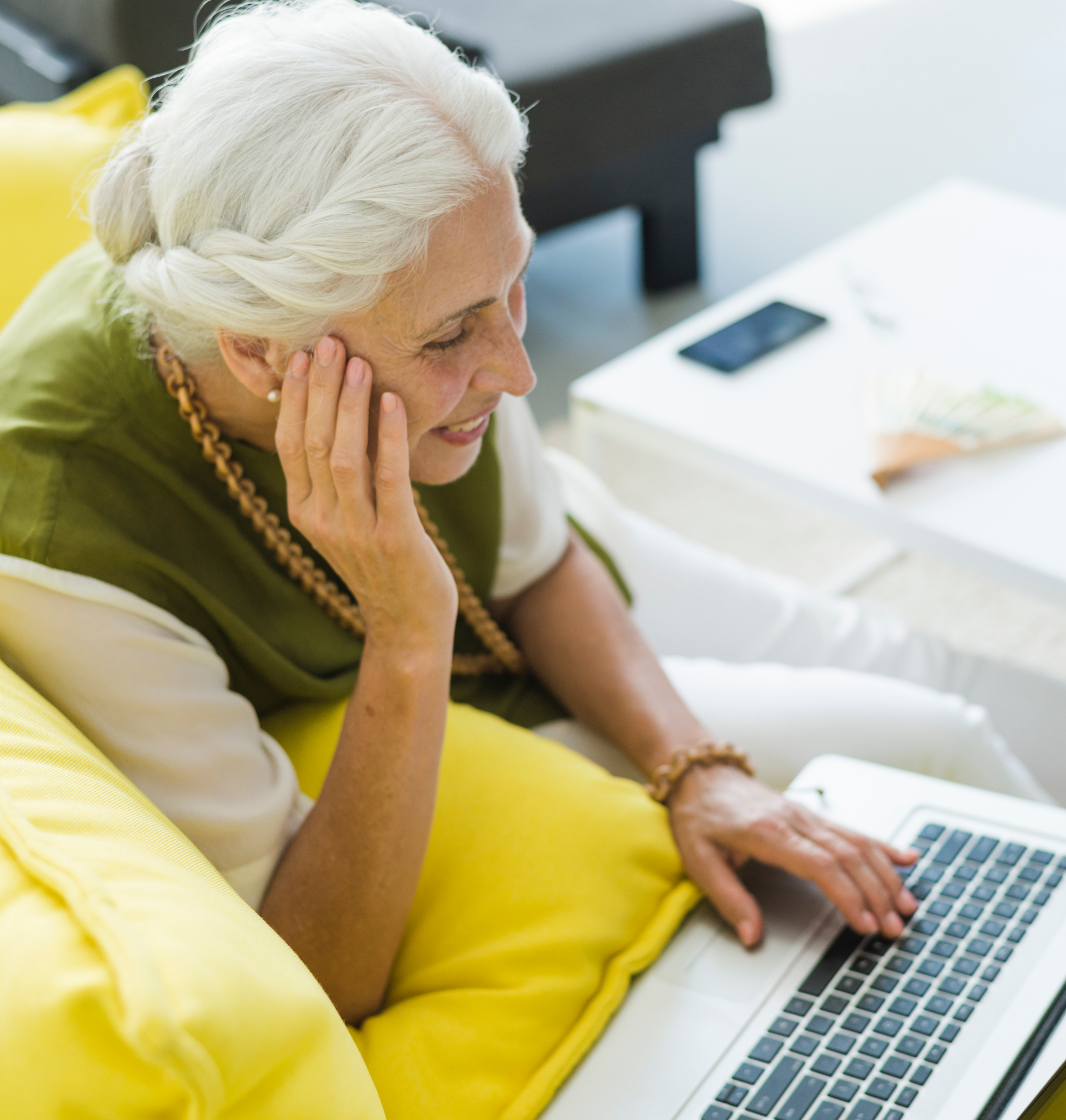 Older woman uses laptop while relaxing on the couch at home