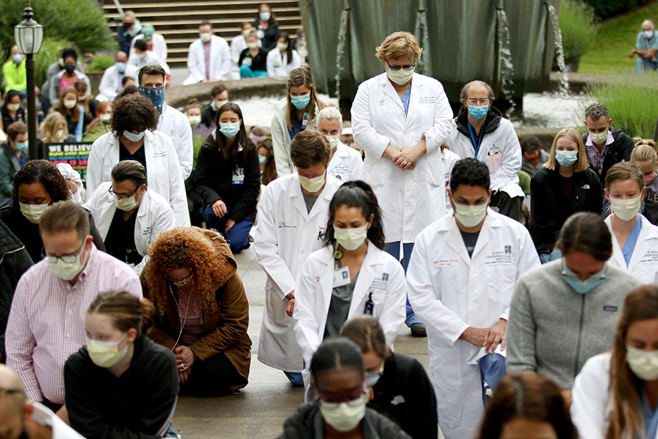 OHSU researchers, scientists and clinicians in white lab coats, many kneeling, heads bowed, wearing protective face masks