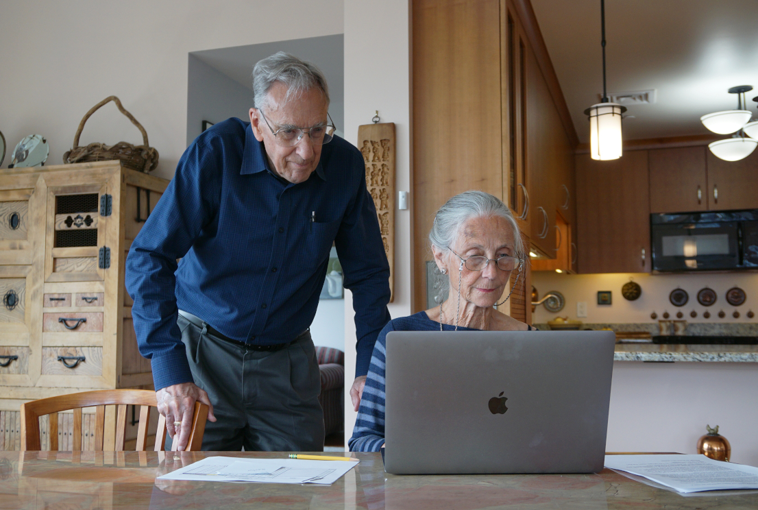 Two older adults look at their computer in the living room of their apartment