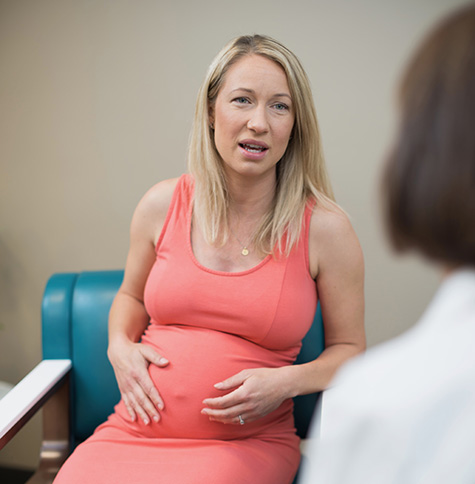 A pregnant patient sitting down and talking with a female doctor.