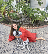A woman in her graduation gown lying on the ground hugging her dog.