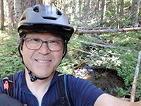 A photo of Bill Chang wearing a helmet on a forest trail.
