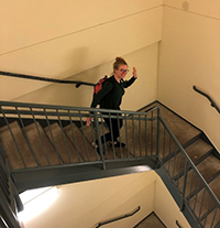 A photo of Kristina Haley waving as she walks down a flight of stairs.