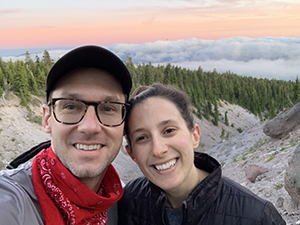 A man and a woman smiling taking a selfie while on a hike.