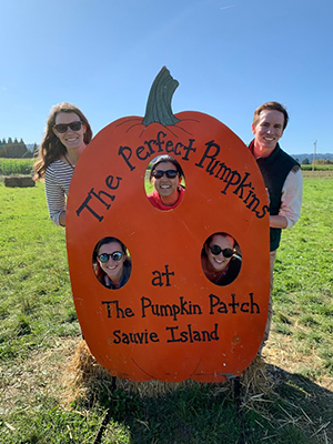 Four girls and one boy pose in a cut-out pumpkin at a pumpkin patch.