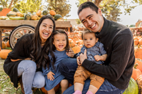 A man and woman crouching down smiling with their two kids at the pumpkin patch.