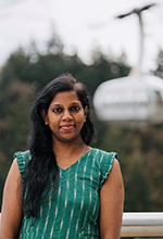A photo of Dhana Angappan standing outside with the OHSU Aerial Tram in the background.