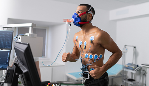 A man wears censors on his chest and stomach and a mask to monitor his breathing while he runs on a treadmill.