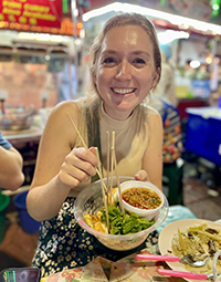 A photo of a woman sitting and eating at a restaurant marketplace.
