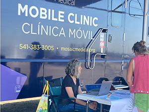 Two people sit at a table in front of the Mobile Clinic