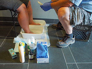 Two sets of legs and feet are shown, one pair is receiving a foot bath and is surrounded by medical supplies