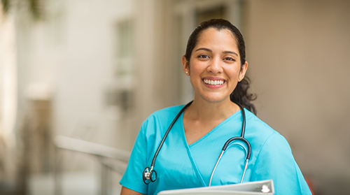 Smiling female healthcare professional looks at the camera while in hospital hallway.