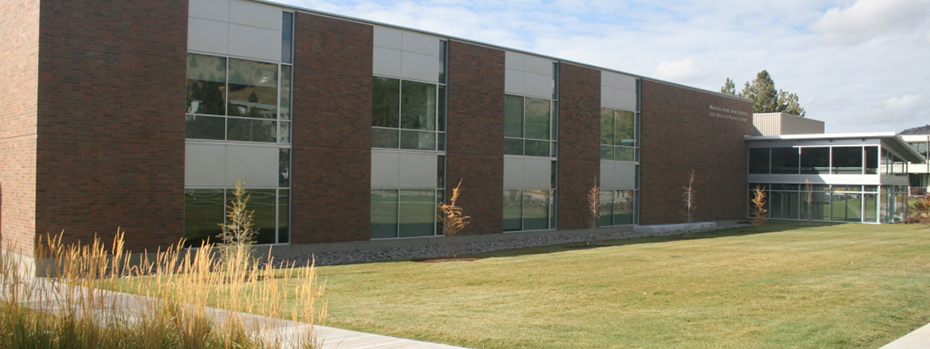The Klamath Falls campus building framed with grass and tall plants on a sunny day.