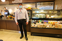 An OHSU employee wearing a face mask stands in front of a coffee bar and food display case. 