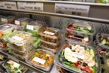 Clear takeout containers filled with various salads sit in a display case.