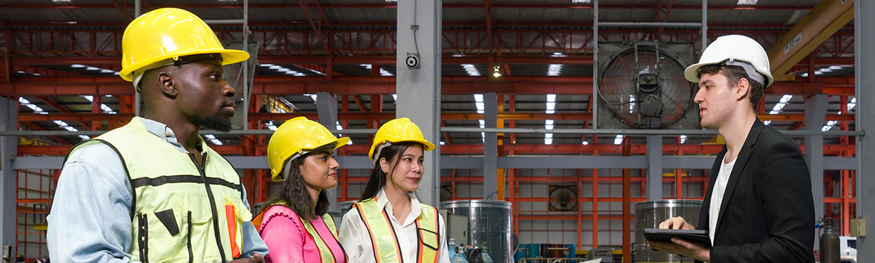 Group of engineer in safety vest meeting with young manager in black suit in an industrial or factory setting.