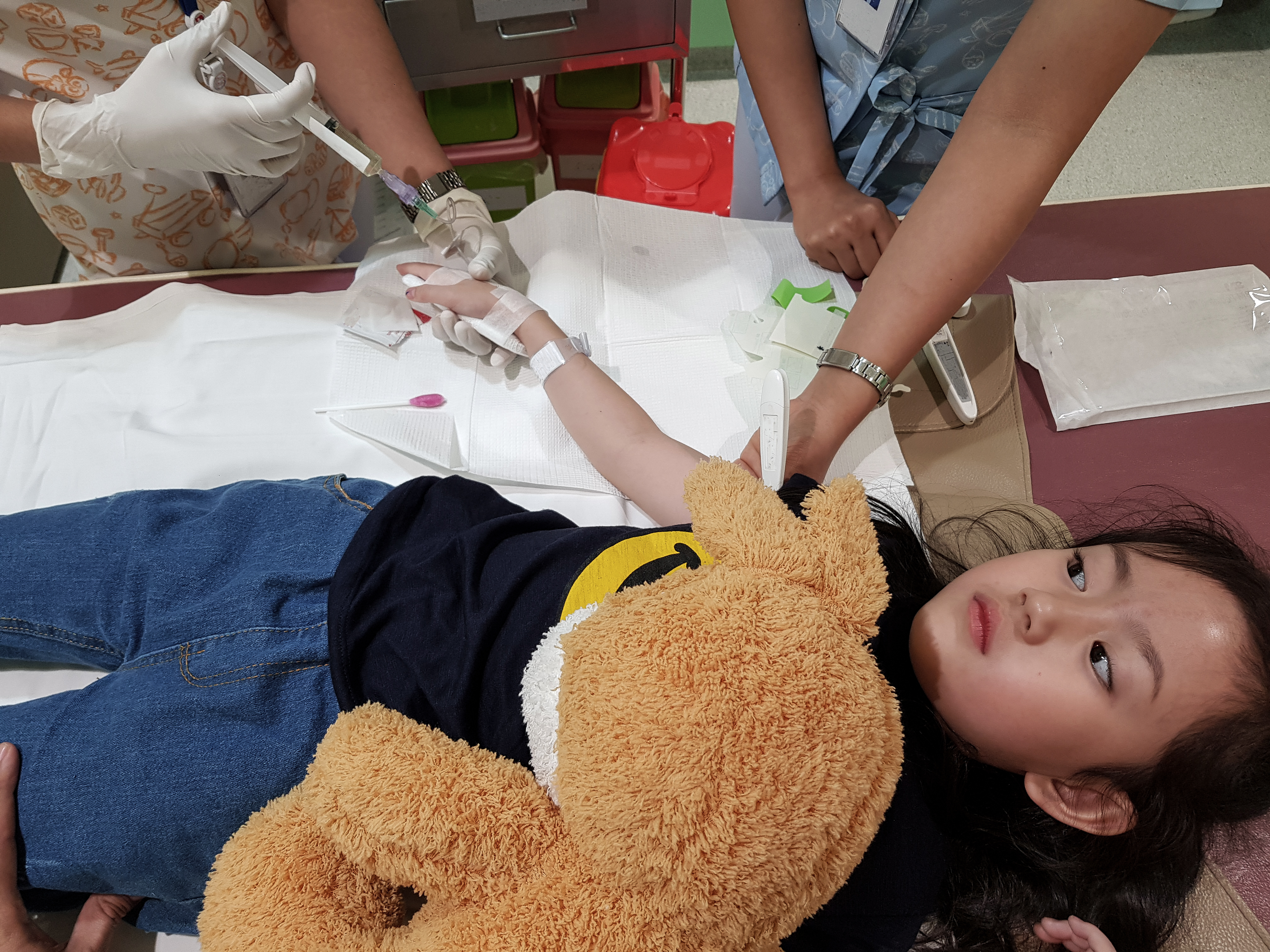 child with stuffed animal lying down while brine is injected by two nurses