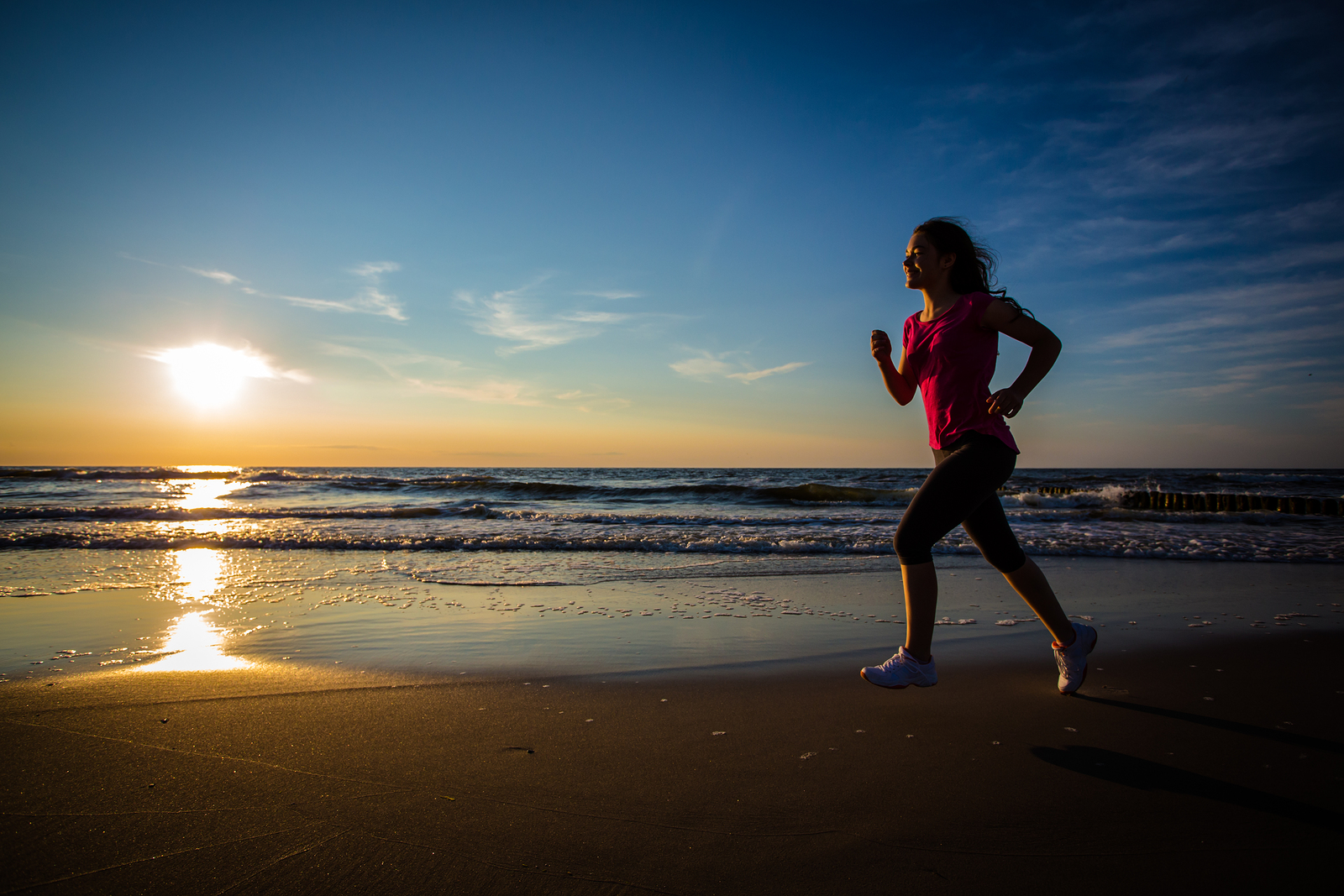 Teen girl running on the beach near sunset