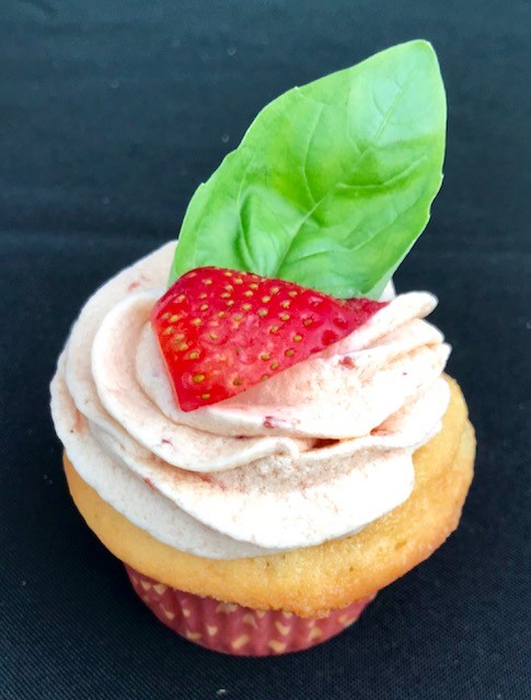 Cupcake with vanilla frosting, a slice of strawberry and a basil leaf on top