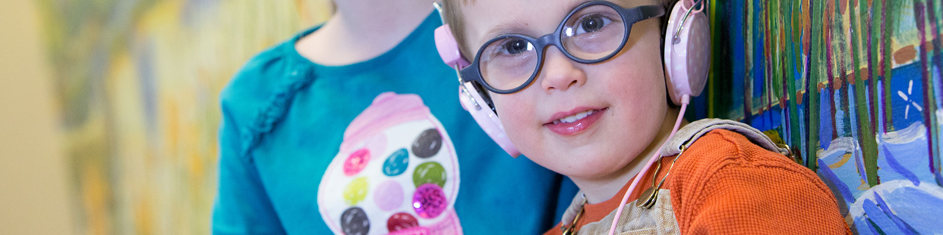 Child with headphones on, smiling, another child behind him.