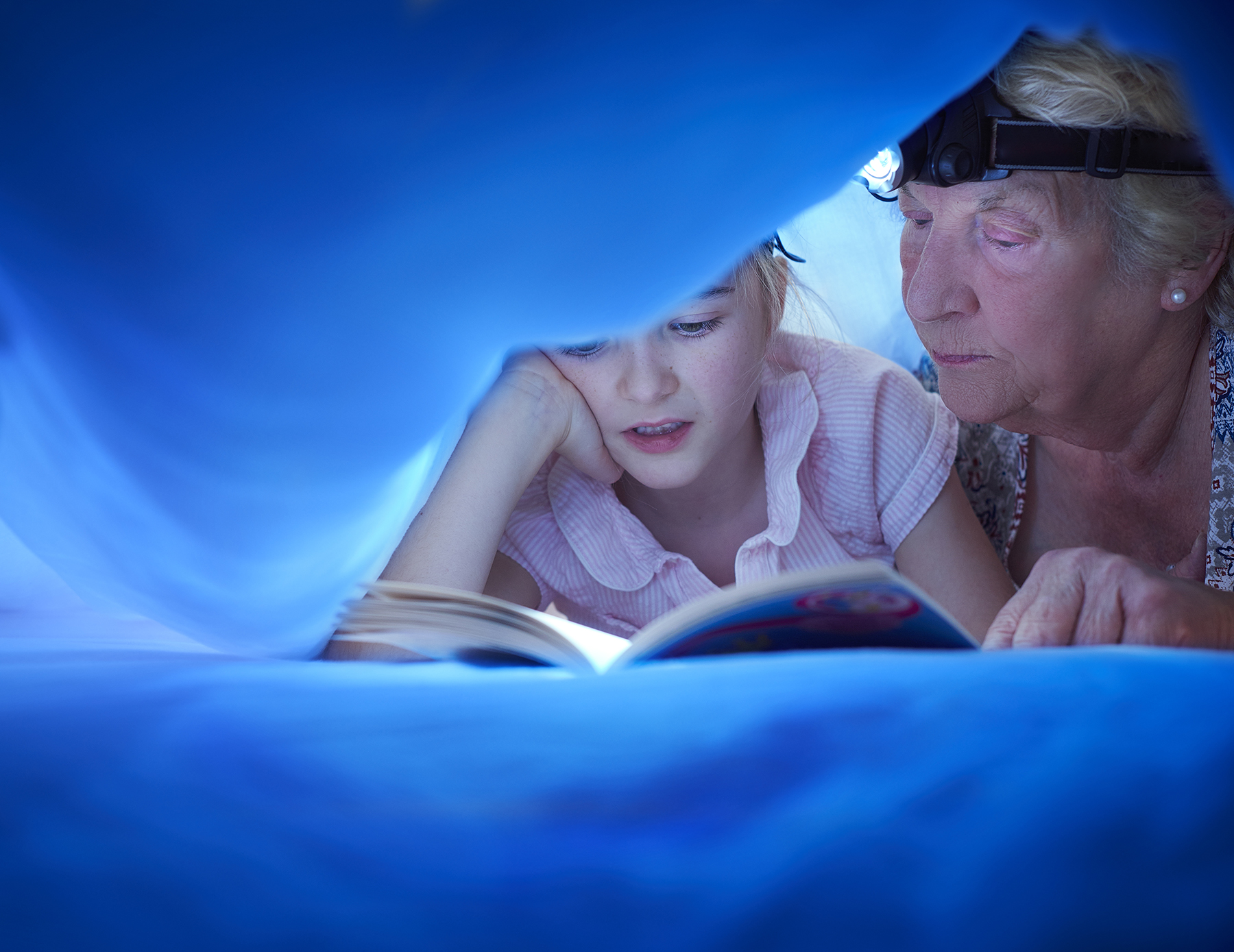 Grandmother reading to her grandchild under a blue fort