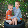 A photo of two young boys embracing while sitting on a car tire outside.