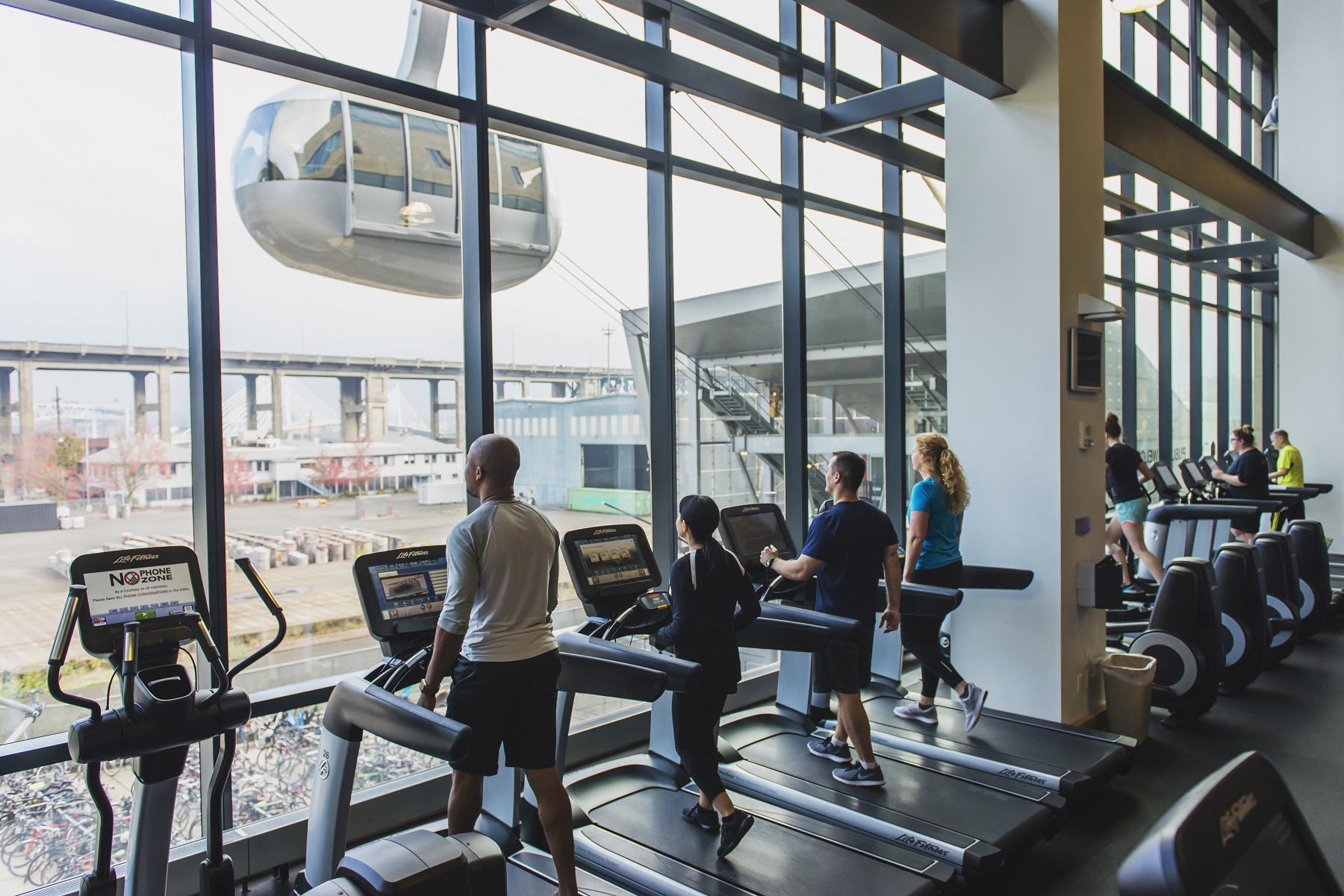 View of Portland Ariel Tram and treadmills from front windows of the fitness floor at march wellness & fitness center.