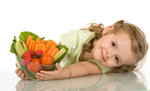 A little girl smiling holding a bowl full of vegetables.