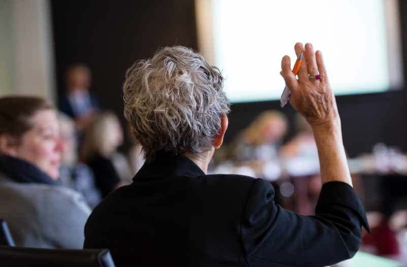 Seen from back, woman holds up hand during meeting